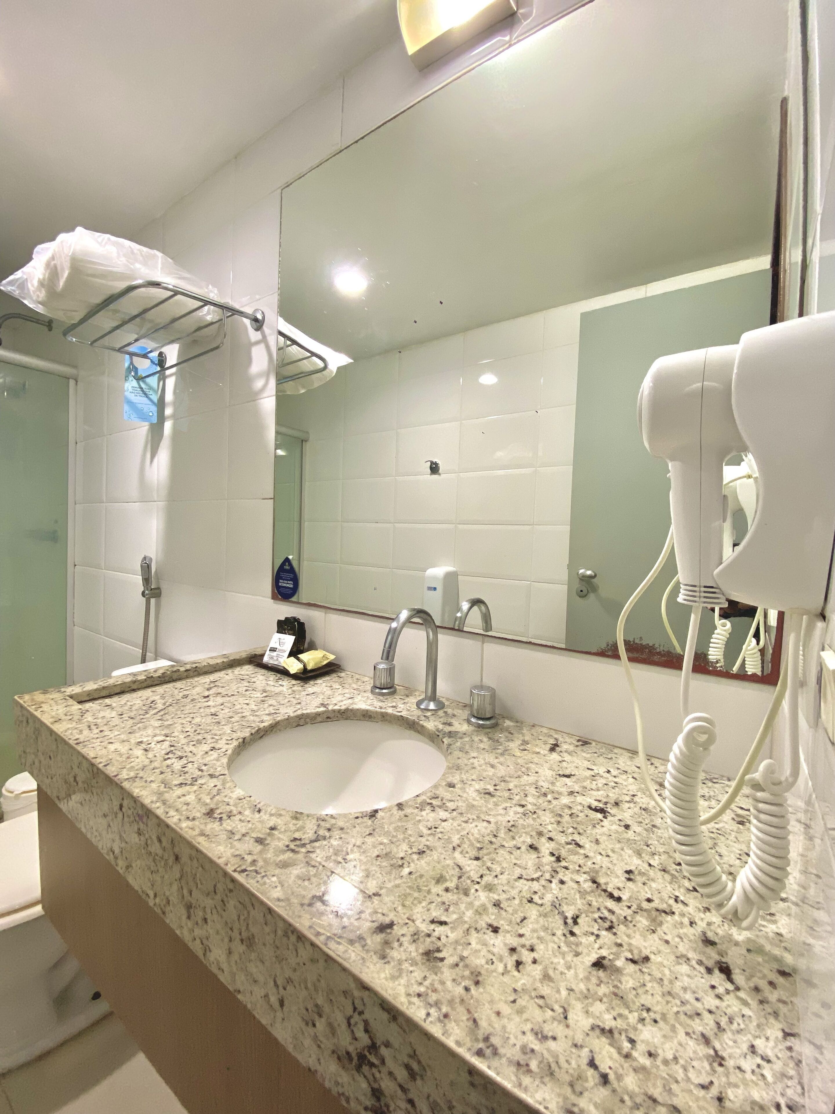 A bathroom with a granite countertop, a sink, a mirror, a hairdryer, and a towel rack.