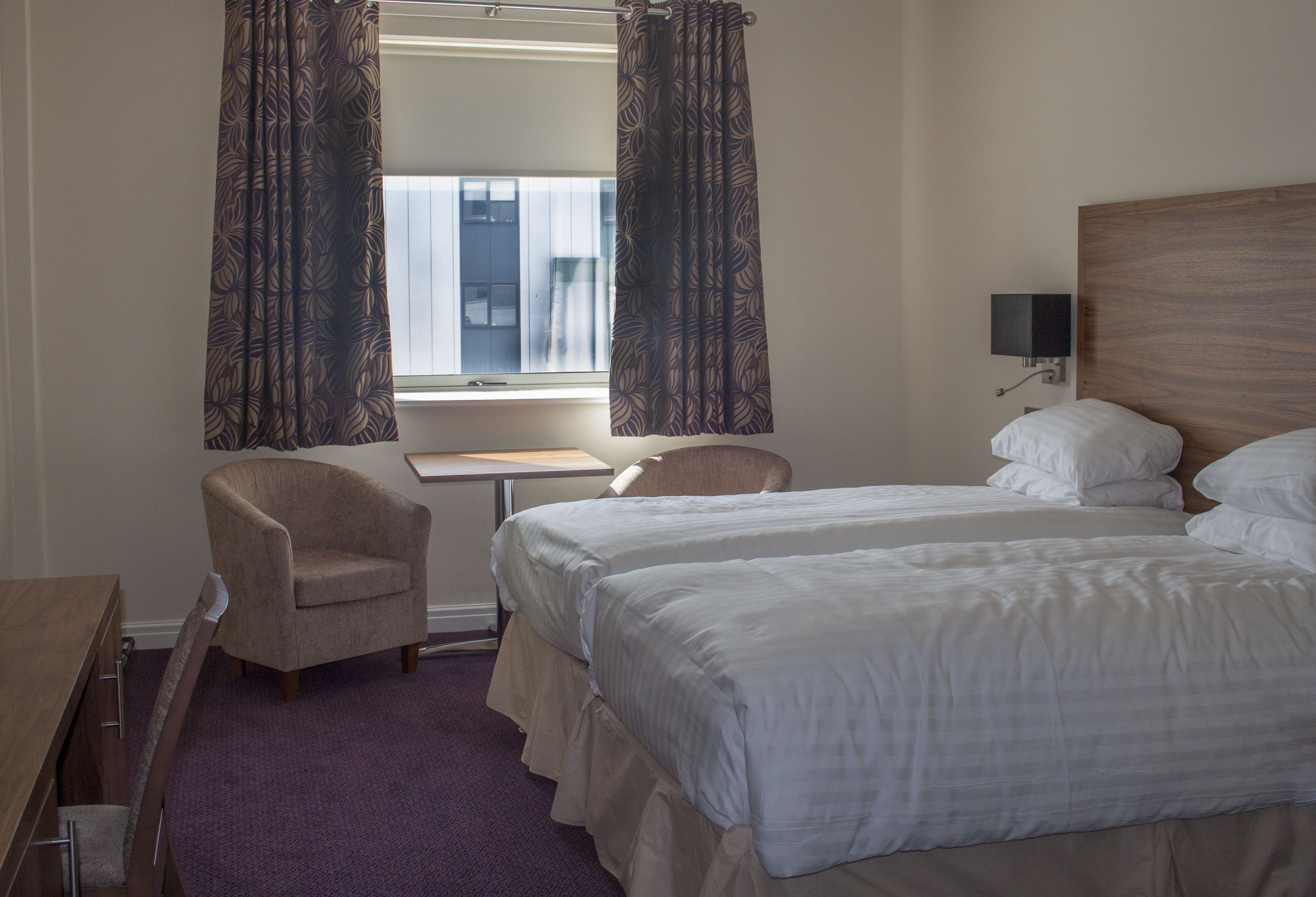 A hotel room with two beds, a desk, a chair, and a window with curtains.