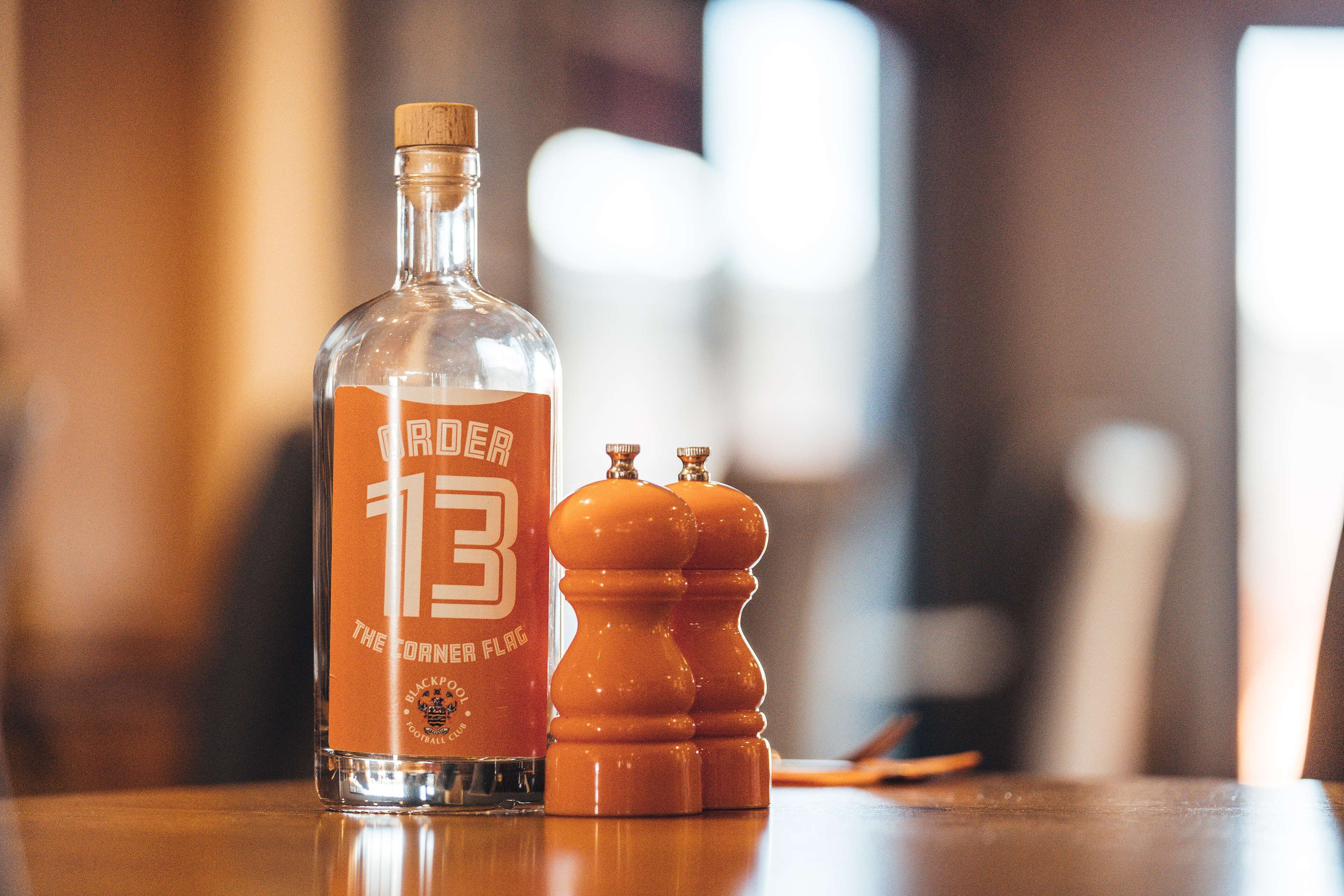 A bottle labeled "The Corner Flag" and two salt and pepper shakers on a wooden table.