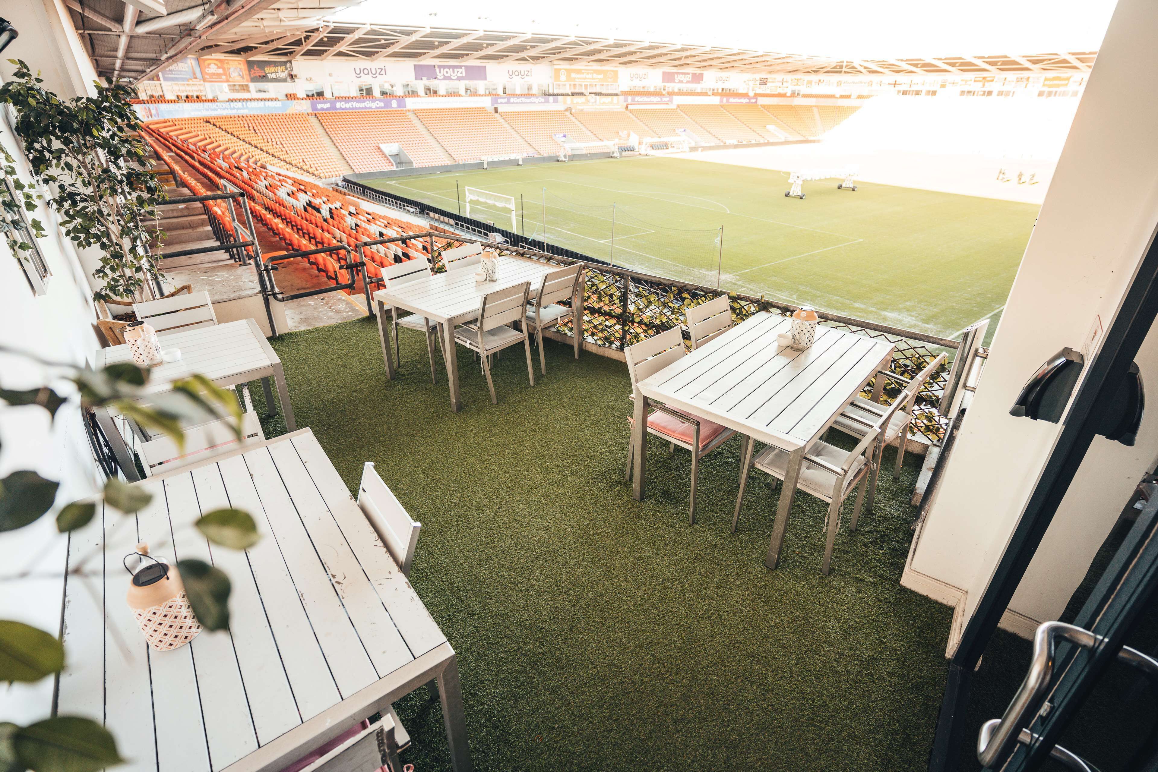 Een stadion met lege oranje stoelen, een grasveld en tafels met stoelen voor het uitzicht.