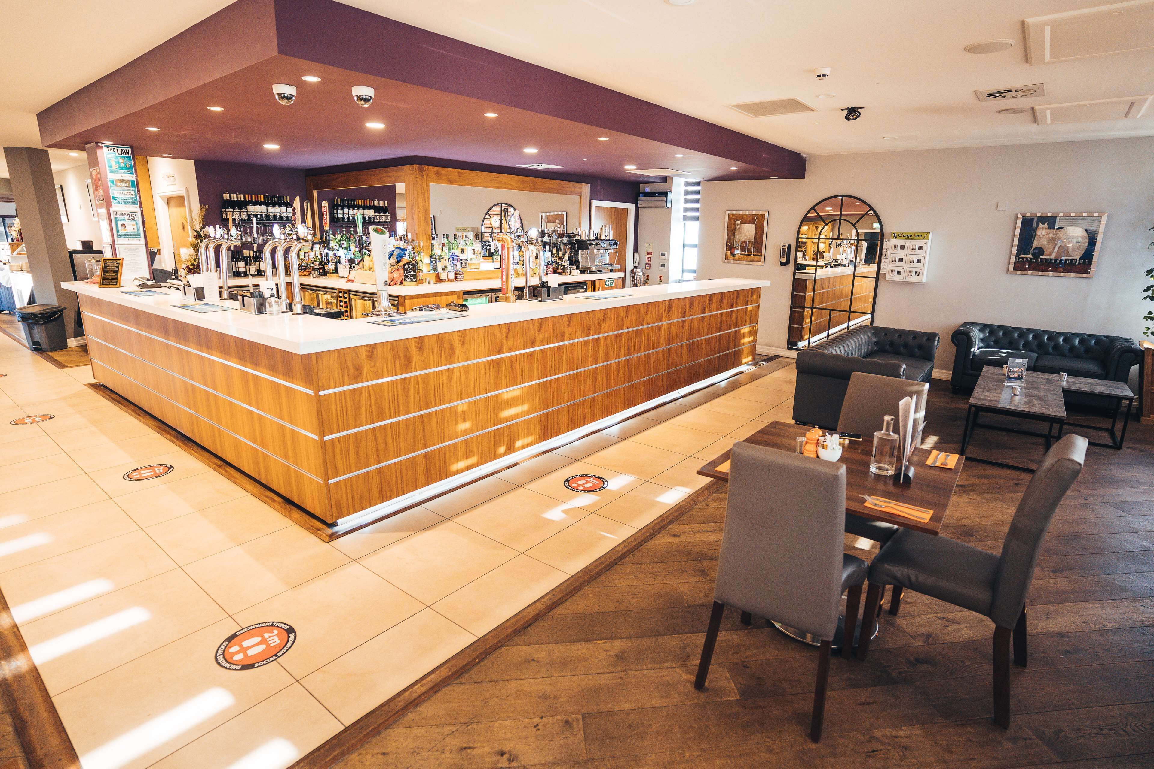 A bar area with a wooden counter, seating with tables and chairs, and a tiled floor with directional markers.