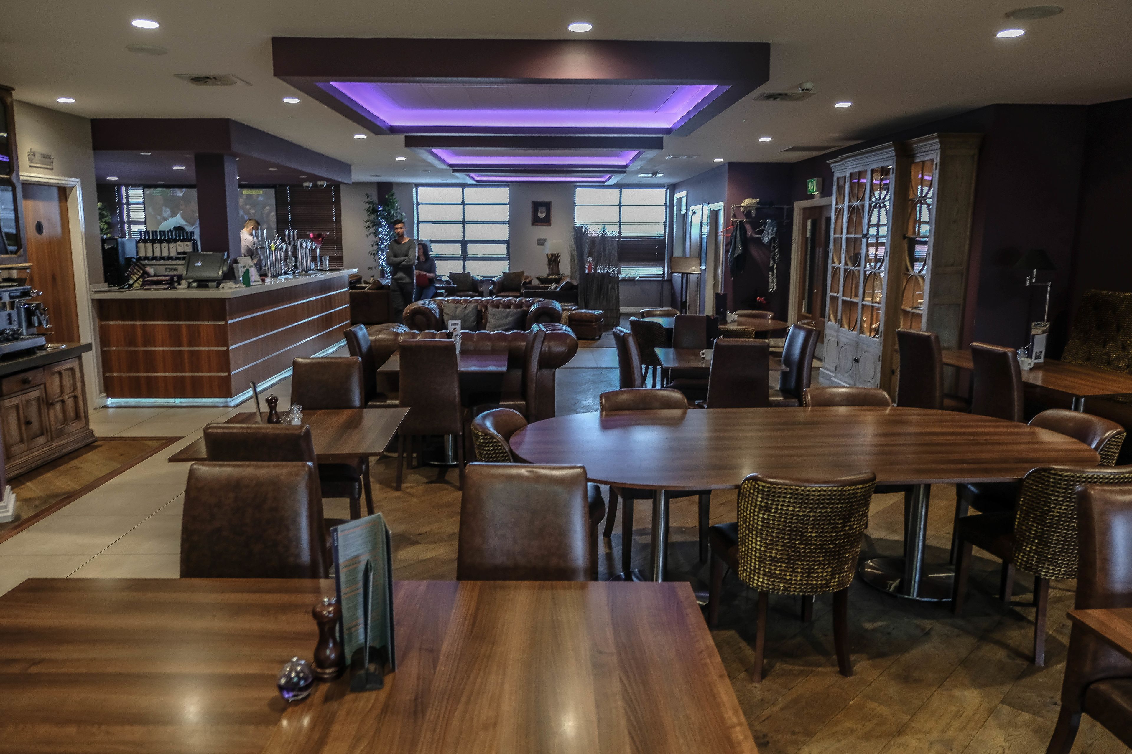 A restaurant with wooden tables and chairs, a bar area, and large windows.