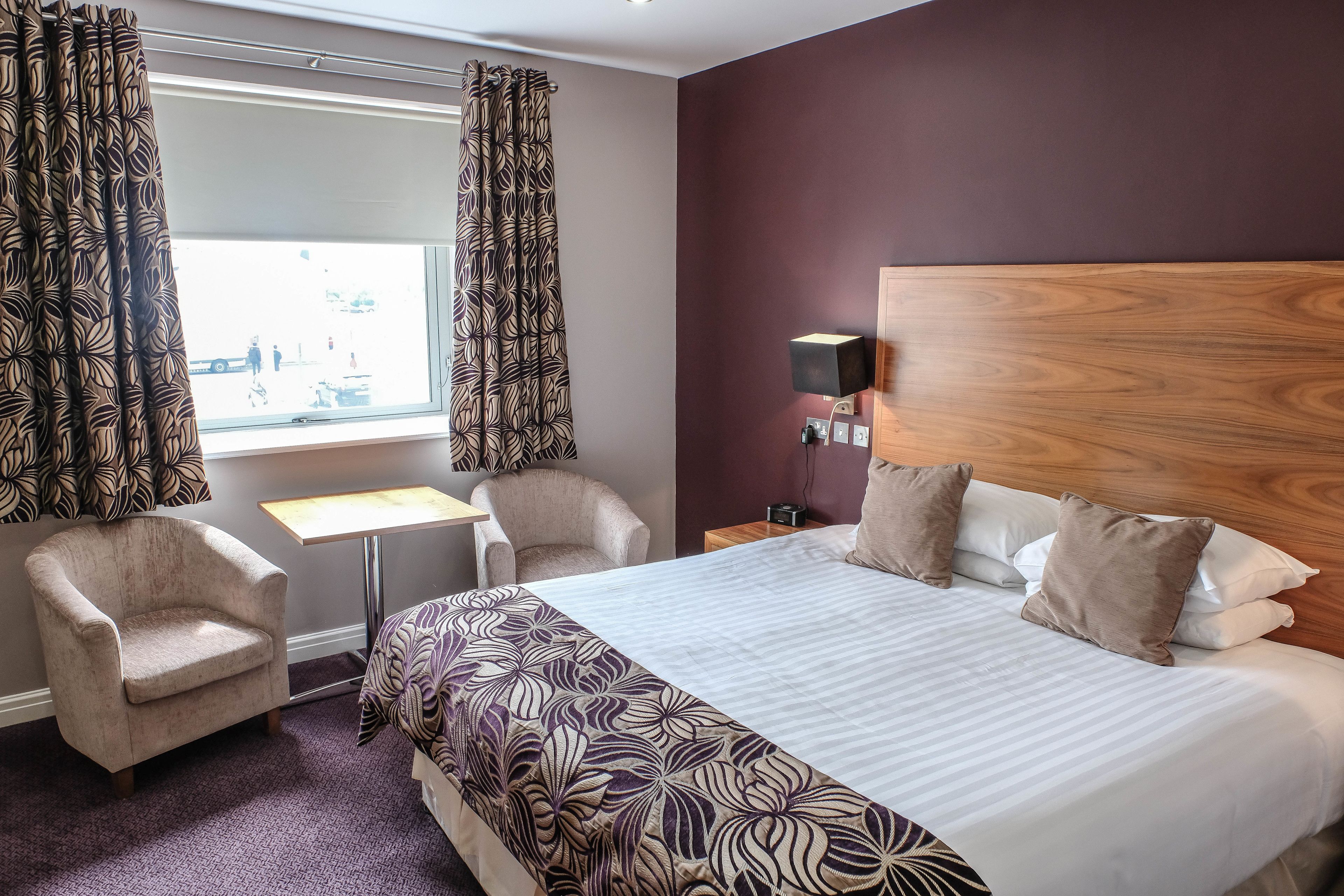 A hotel room with a large bed, two armchairs, a small table, and a window with curtains.