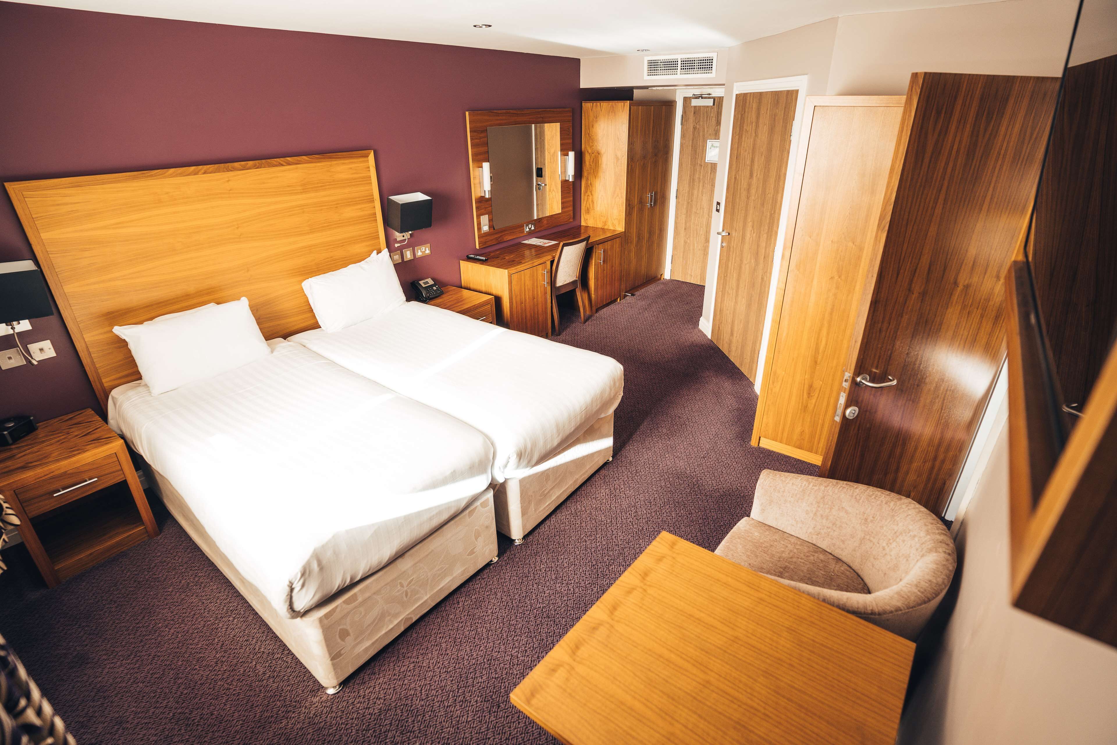 Une chambre d’hôtel avec deux lits, un bureau, une chaise, une armoire et un miroir.