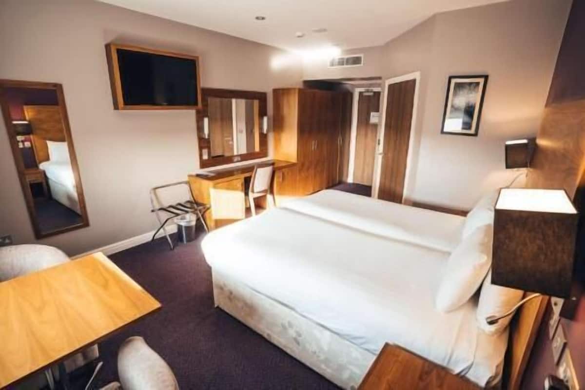 A hotel room with a bed, a desk, a chair, a mirror, and a television.