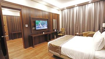 A hotel room with a large bed, a television mounted on the wall, a seating area with a chair and a small table, and a wardrobe.
