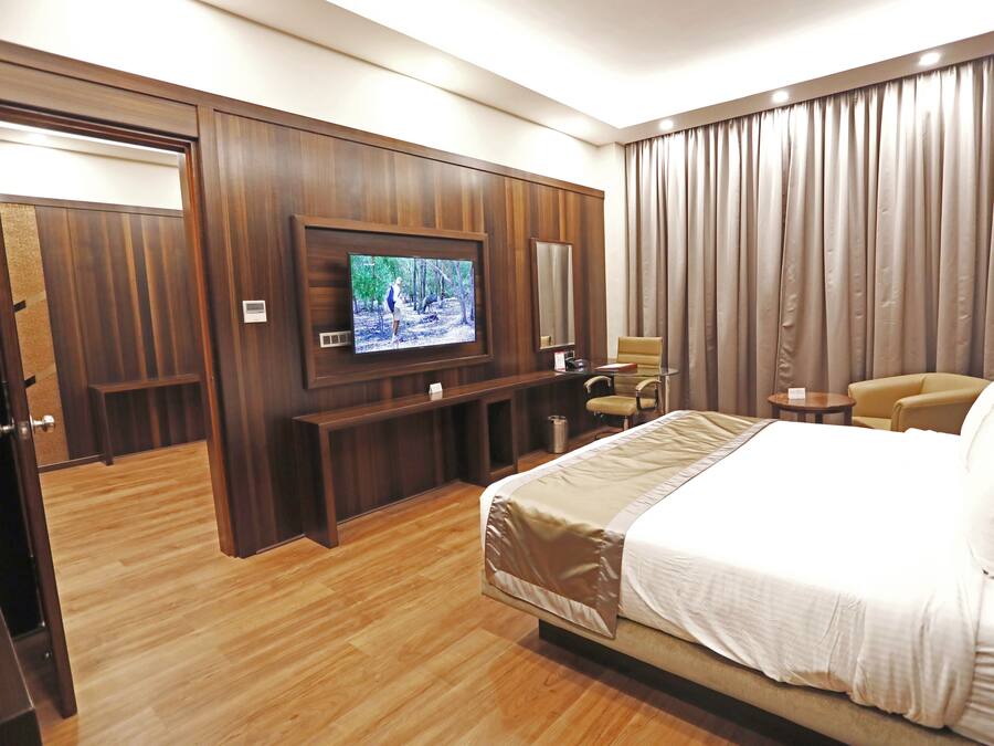 A hotel room with a large bed, a television mounted on the wall, a seating area with a chair and a small table, and a wardrobe.