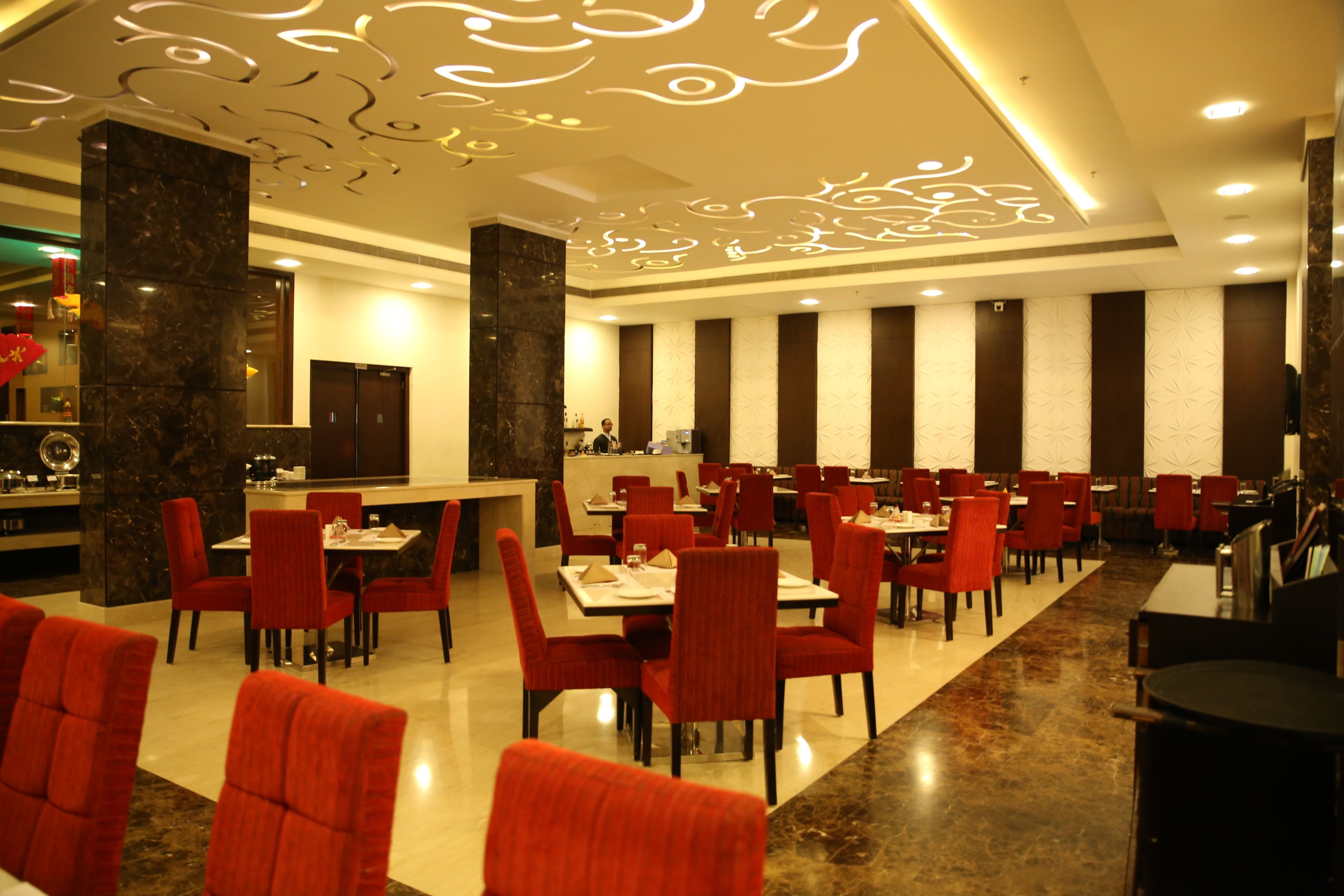 A spacious dining area with red chairs and tables, a marble column, and a modern ceiling design.