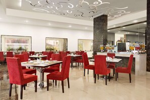 Uma sala de jantar moderna com cadeiras estofadas em vermelho e mesas, piso de mármore e um bar central com bancada de granito.