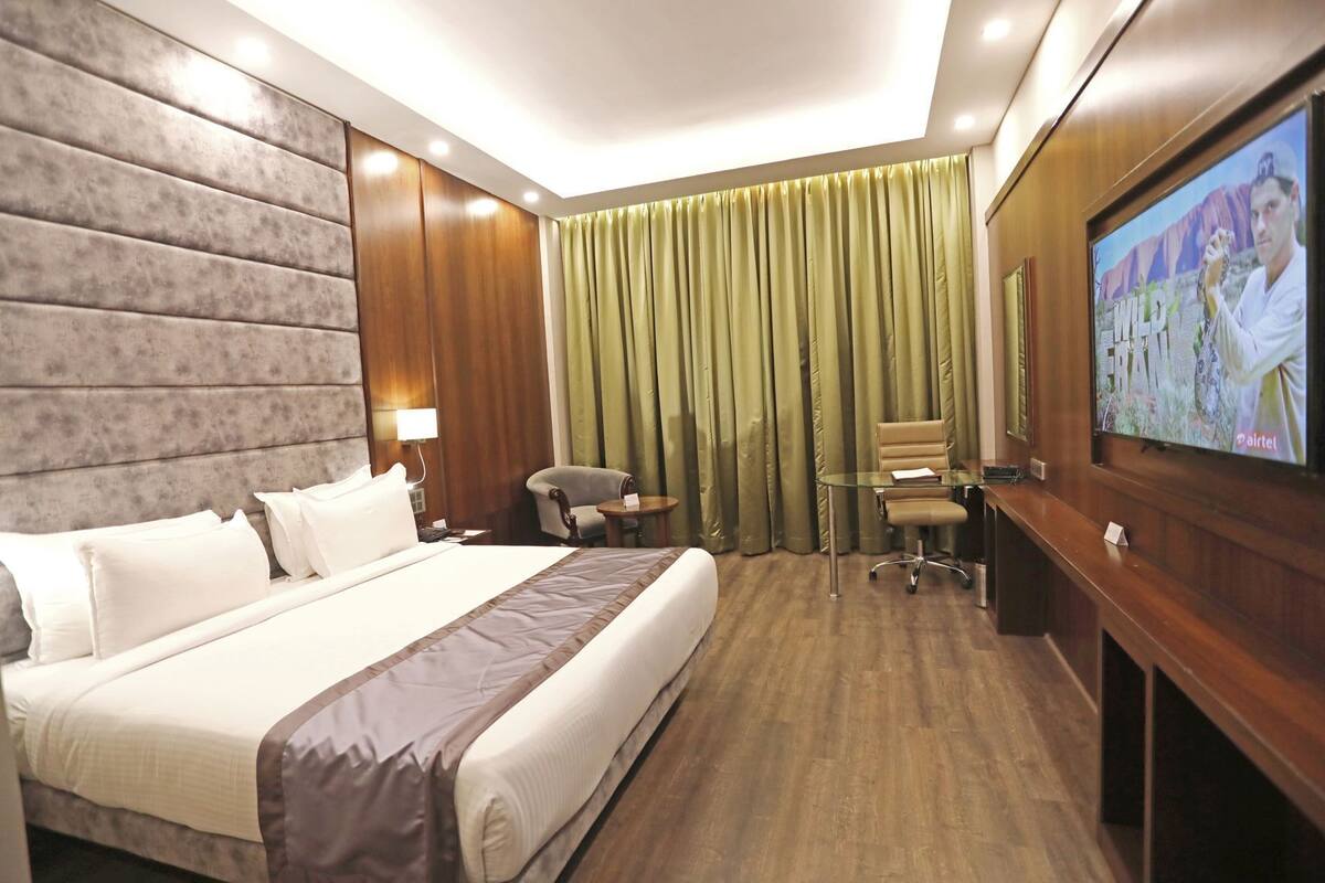 Una habitación de hotel con una cama grande, un escritorio con silla, un televisor y una ventana con cortinas.
