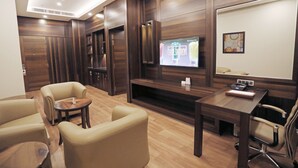 Quarto de hotel moderno com piso de madeira, televisão fixada na parede, escrivaninha com cadeira e um sofá.
