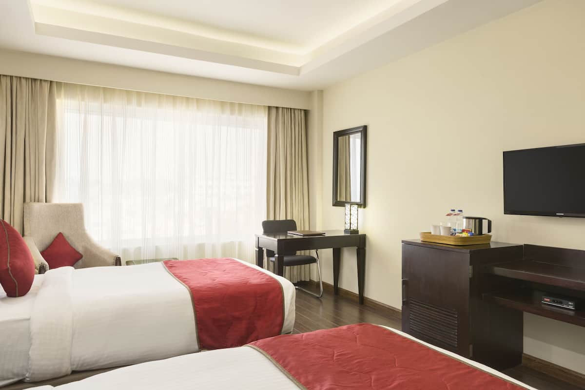 Habitación de hotel con dos camas, un escritorio, una silla, un televisor y una ventana con cortinas.