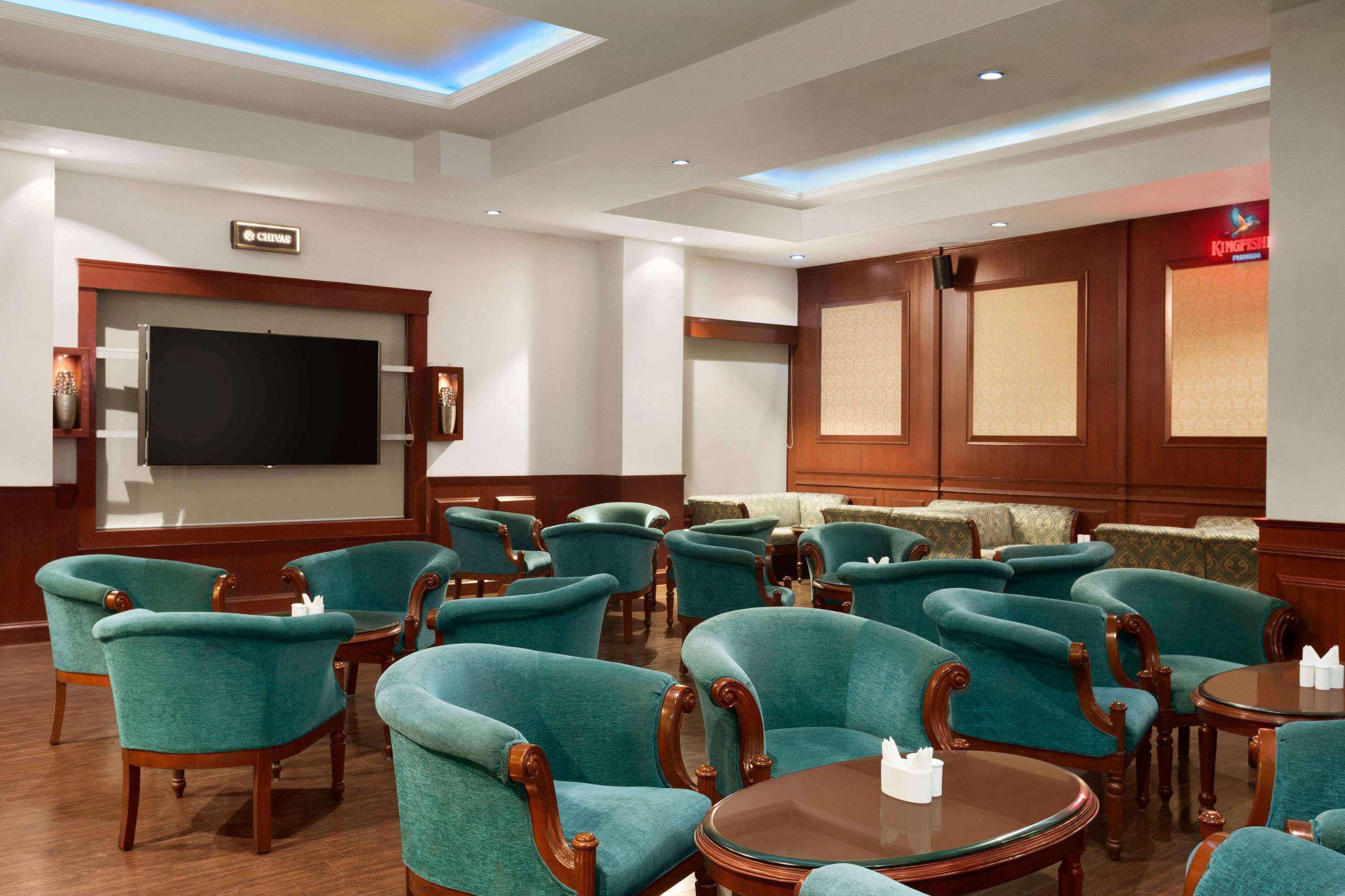 Un vestíbulo de hotel con sillones tapizados en color turquesa, un televisor de pantalla plana grande, paneles de madera y un letrero que dice 'Kingfisher'.