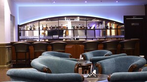 Uma área de bar com balcão curvo, vários bancos altos e um espaço de estar com cadeiras estofadas.
