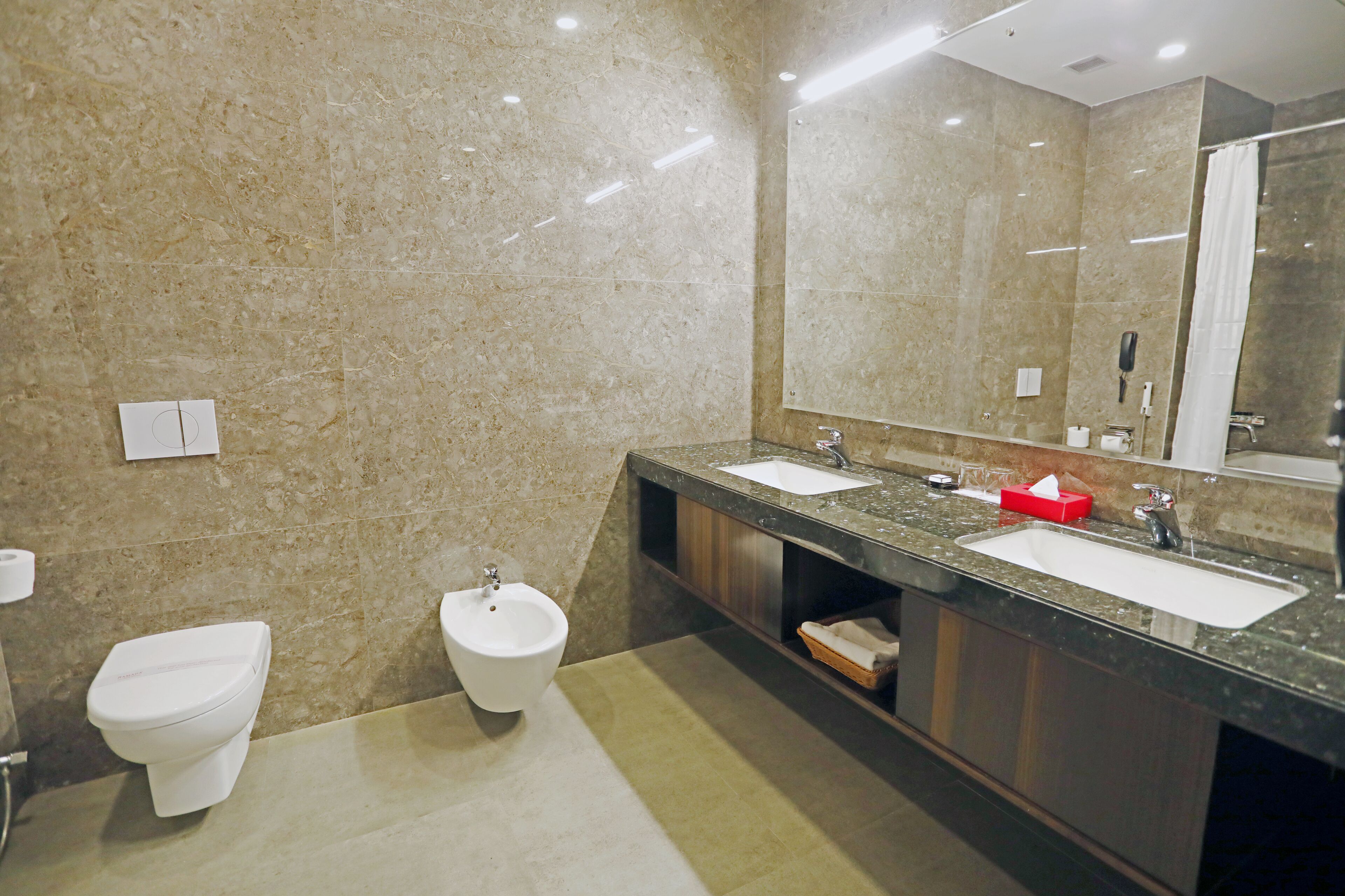 A modern bathroom with two sinks, a bidet, and a large mirror.