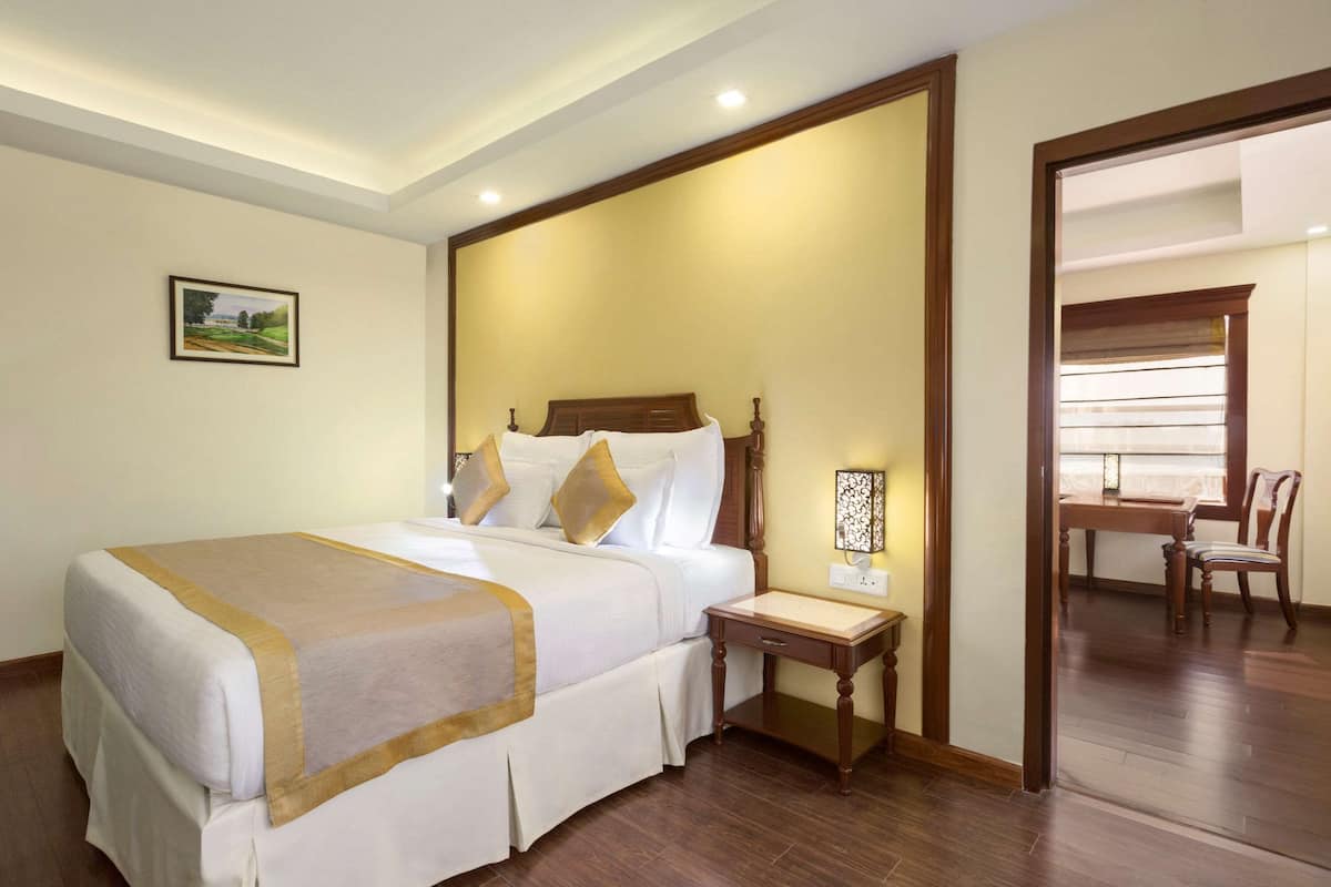 Una habitación de hotel con una cama grande, una mesita de noche, una lámpara y vistas a un comedor.