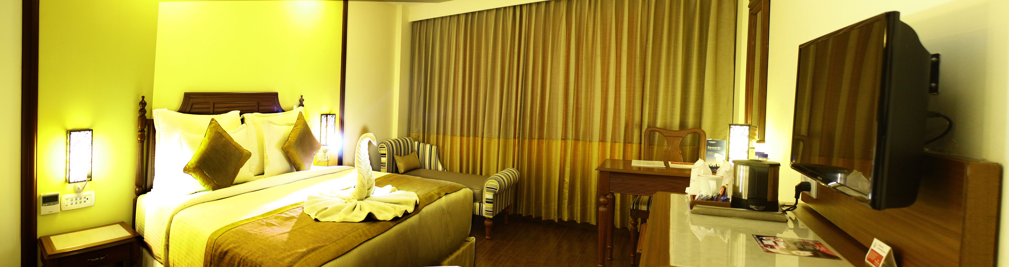 A hotel room with a bed, a bedside table, a chair, a mirror, and a television.