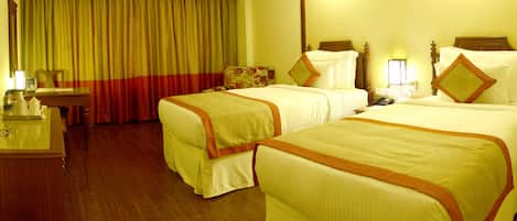 A hotel room with two beds, a desk, a chair, a television, and a window with curtains.