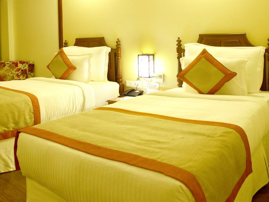 Quarto de hotel com duas camas, uma escrivaninha, uma cadeira, uma televisão e uma janela com cortinas.