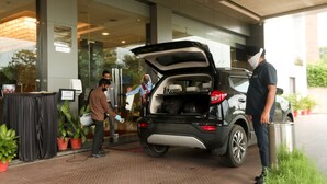 Um carro com o porta-malas aberto, estacionado em frente a um edifício com porta de vidro.