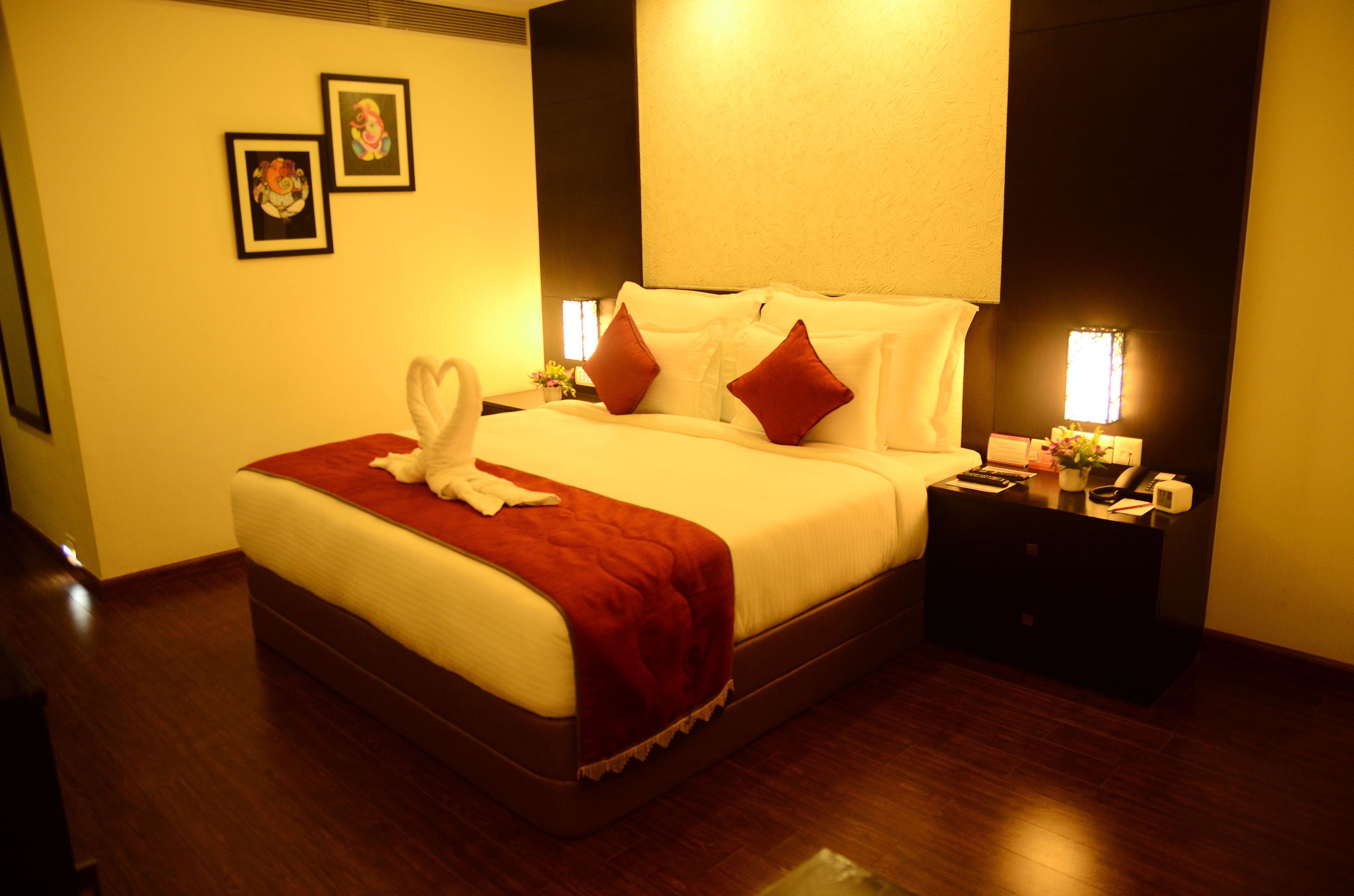 A neatly made bed with a red blanket and white towels, a nightstand with a lamp, and framed pictures on the wall.