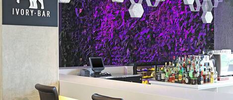 A bar area with a modern design, featuring a hexagonal pattern wall, a counter with a computer, and several stools.