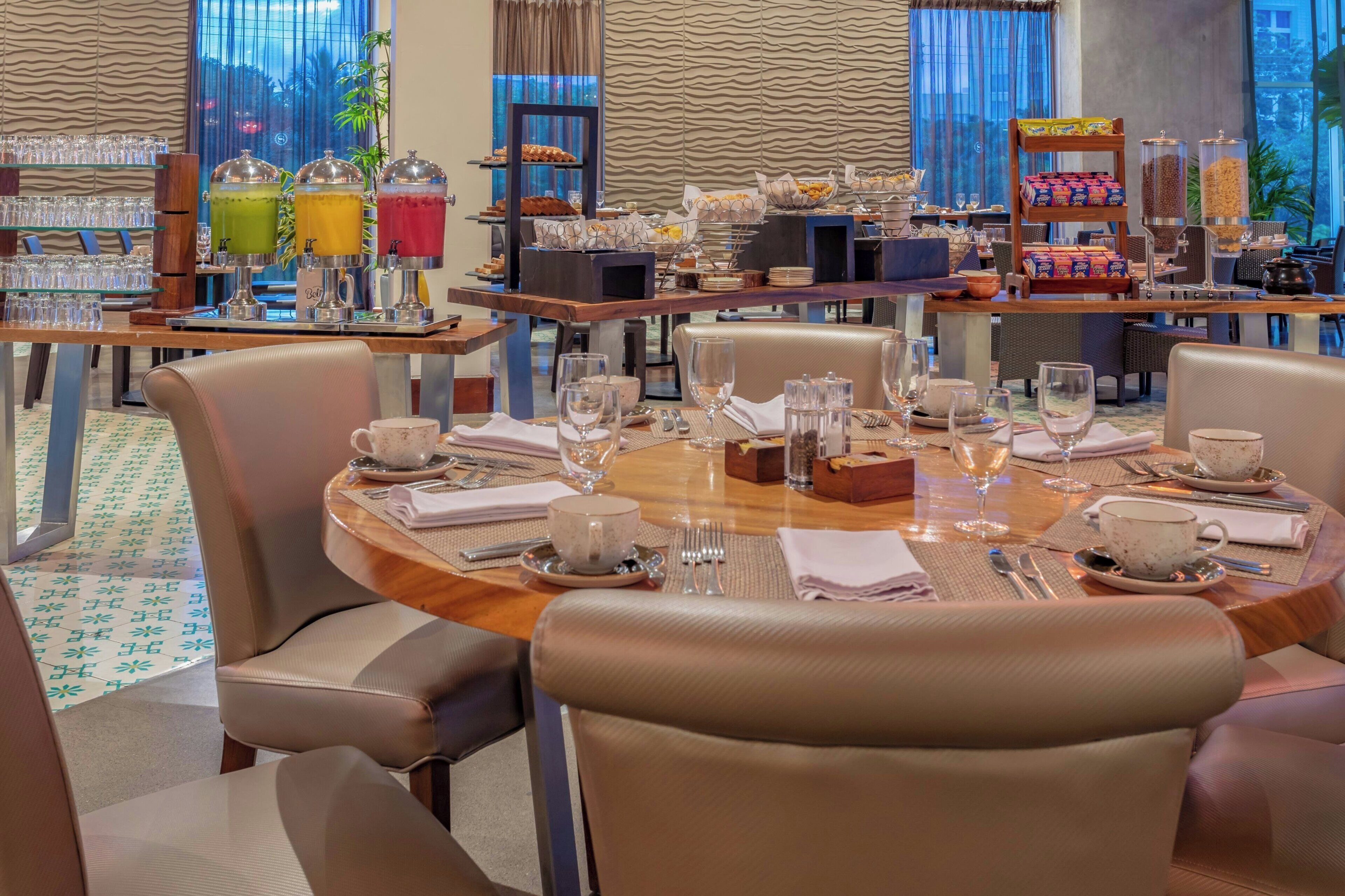 A dining area with round tables, cushioned chairs, and a buffet with various food items.
