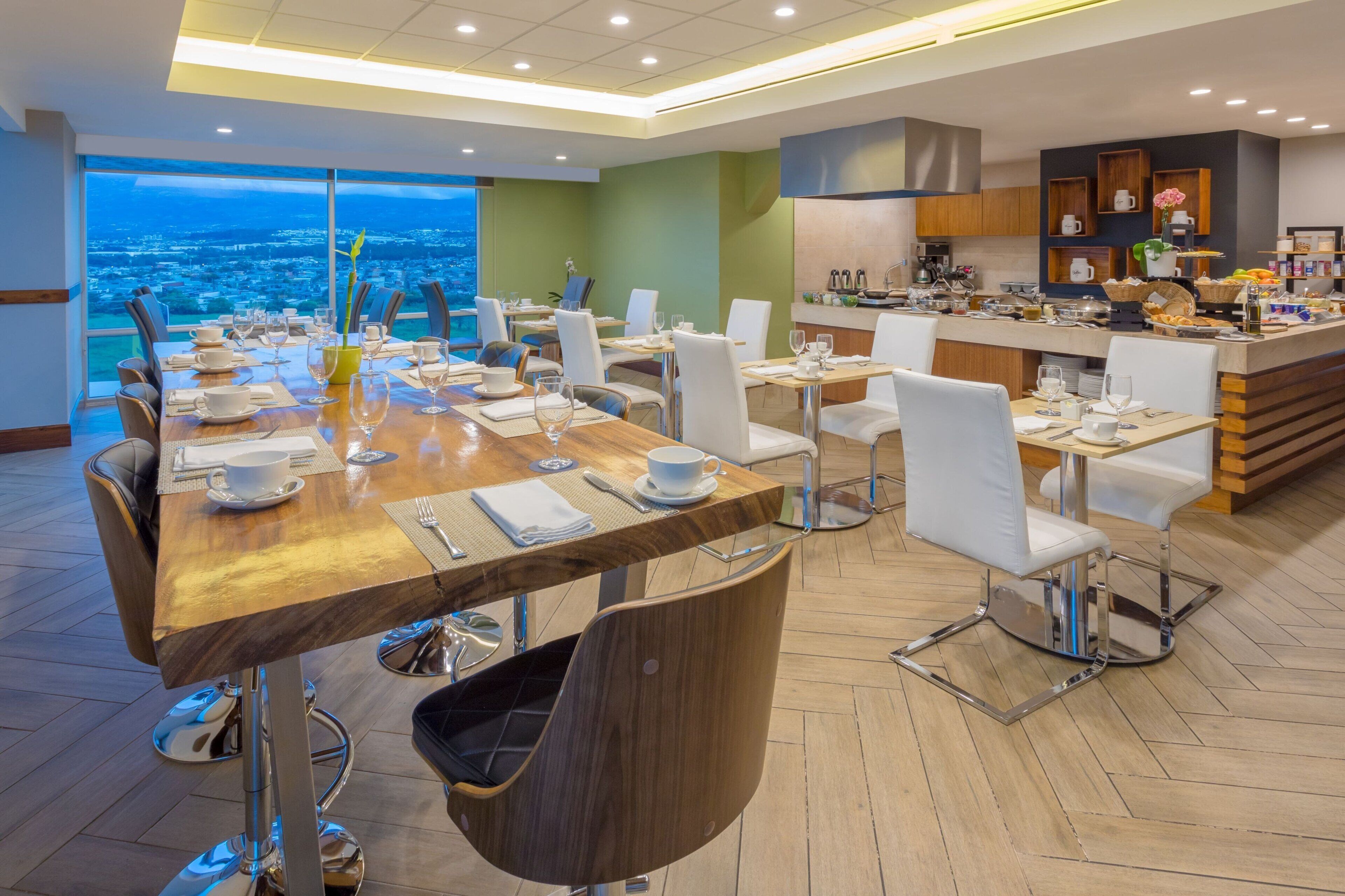 Un comedor moderno con una larga mesa de madera dispuesta para una comida, rodeada de sillas blancas.