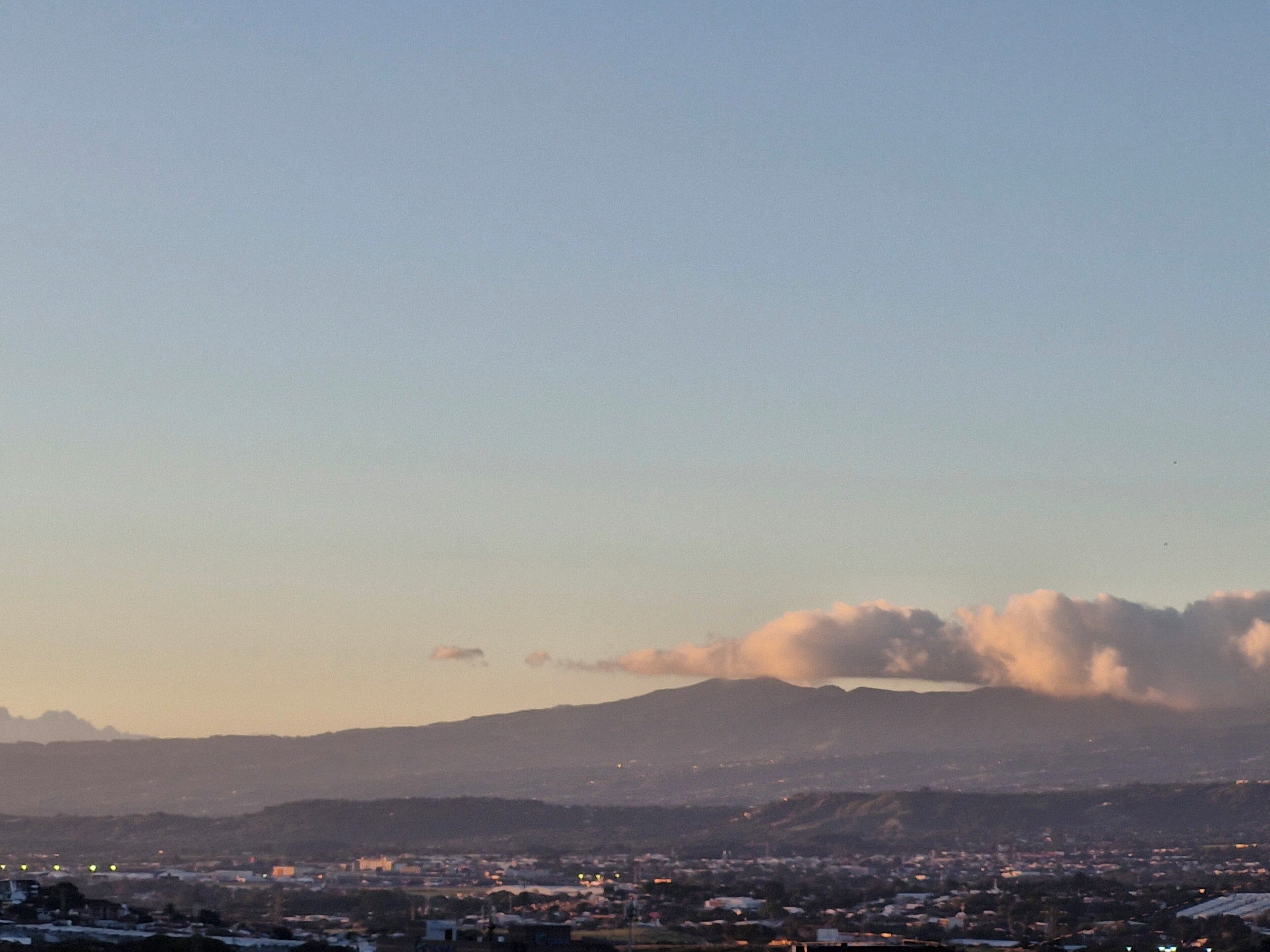 Stadtansicht mit einem Berg im Hintergrund, Gebäuden und blauem Himmel.