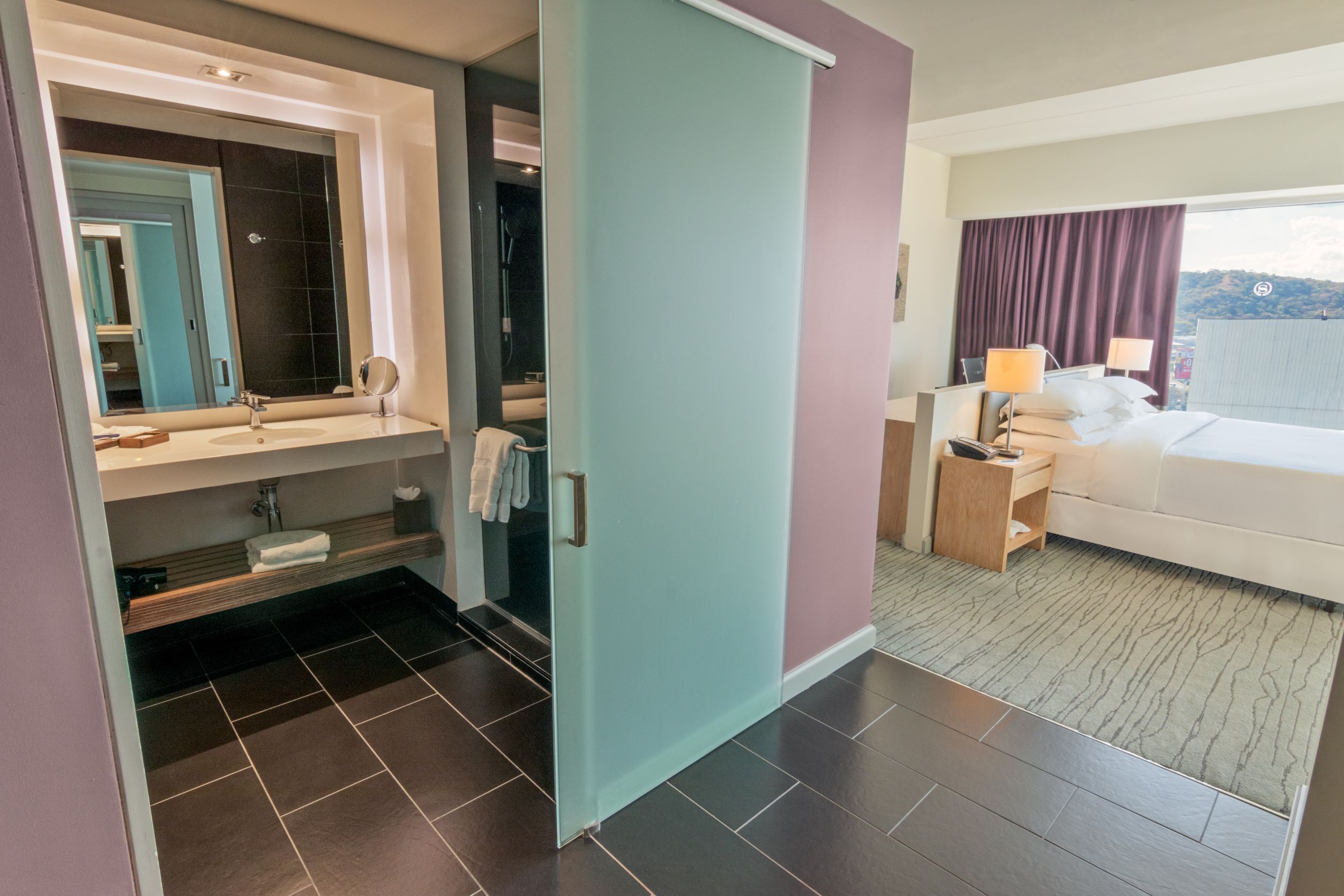 A hotel room with a bathroom, a bed, and a view of the outdoors.