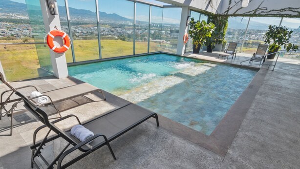 An indoor swimming pool with clear glass walls, a lifebuoy, and lounge chairs.