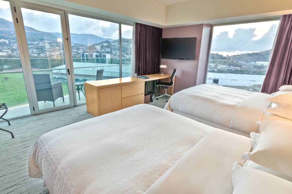 A hotel room with two beds, a desk, and a TV.