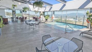 Relax on the rooftop terrace with a glass-enclosed pool, surrounded by lush plants and comfortable seating.