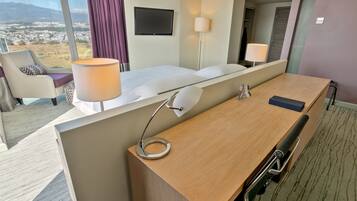 A hotel room with a large bed, a desk, a chair, a lamp, and a TV.