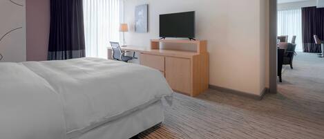 Habitación de hotel con una cama grande, un escritorio con una silla, un televisor de pantalla plana y vistas al pasillo.