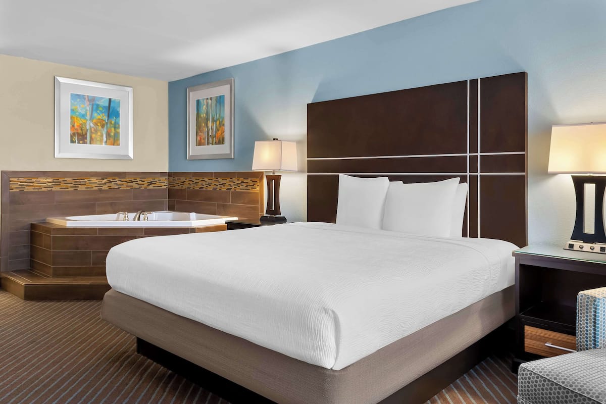 A hotel room with a large bed, a bathtub, a nightstand, and two wall-mounted lamps.