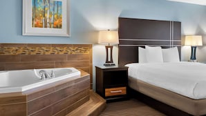 Habitación de hotel con una cama grande, una bañera empotrada, dos lámparas de noche y un cuadro enmarcado en la pared.