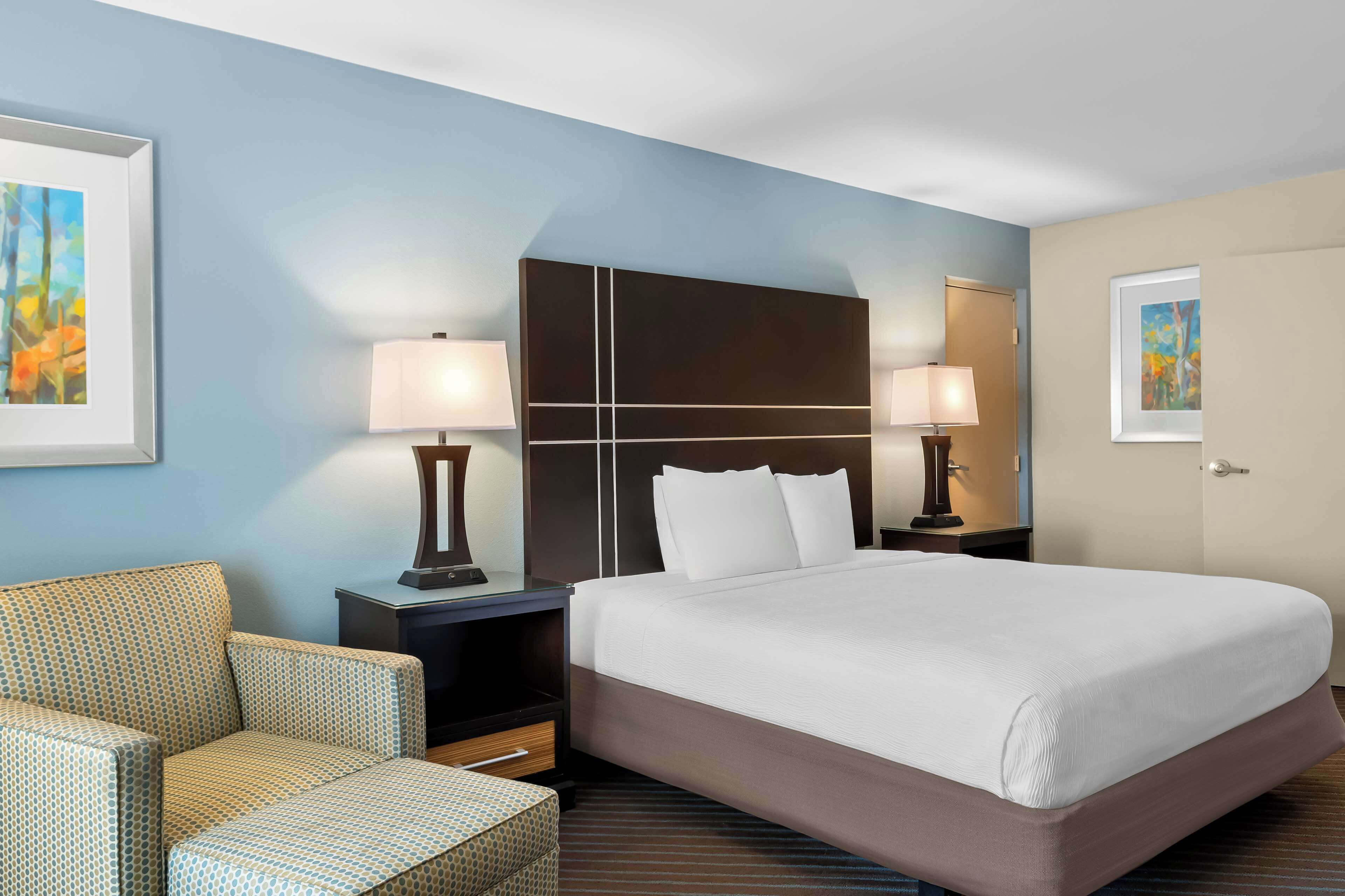 A hotel room with a large bed, two bedside tables with lamps, a sofa, and artwork on the walls.