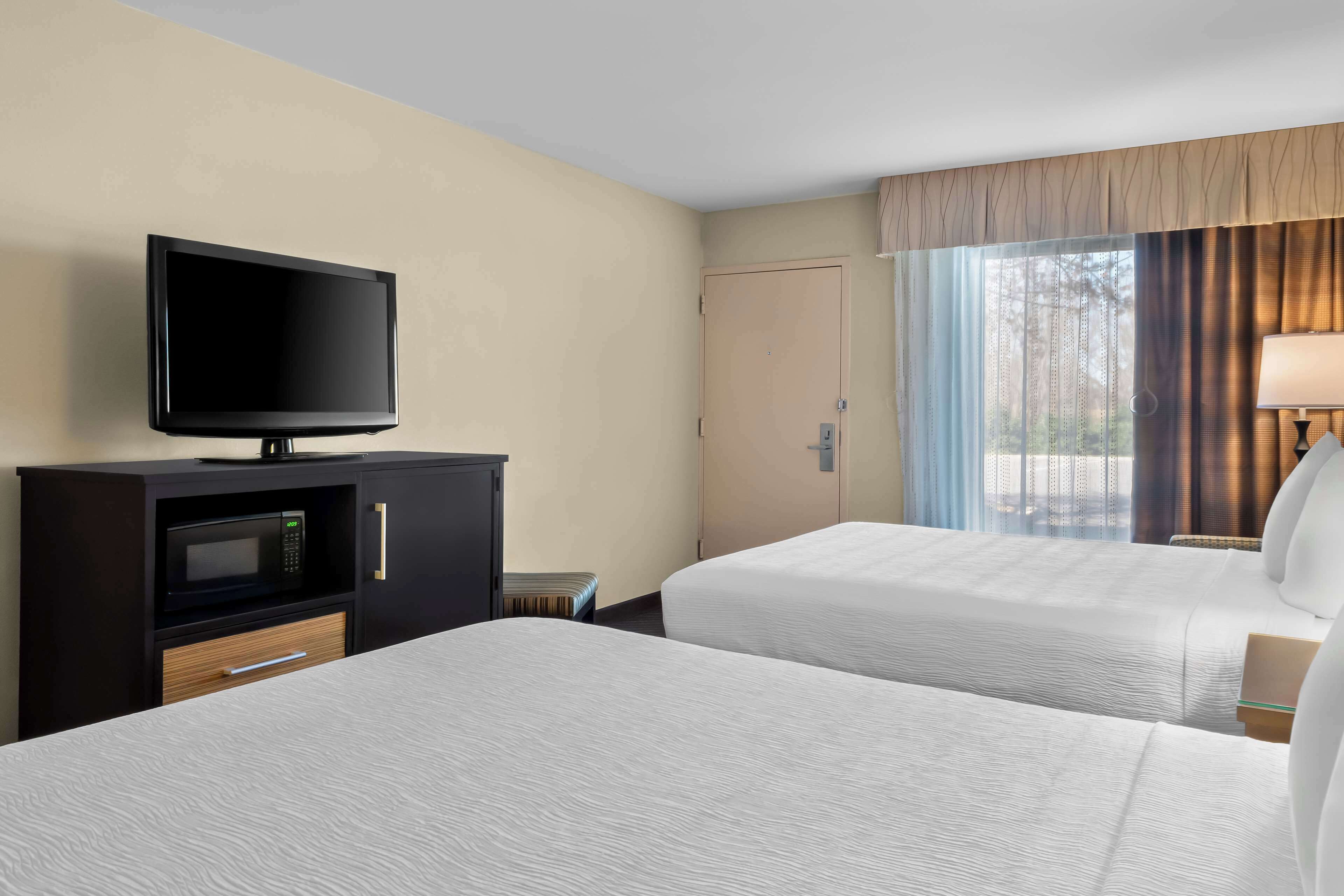 Een hotelkamer met twee bedden, een televisie op een kastje, een magnetron en een raam met gordijnen.