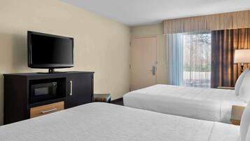 Een hotelkamer met twee bedden, een televisie op een kastje, een magnetron en een raam met gordijnen.