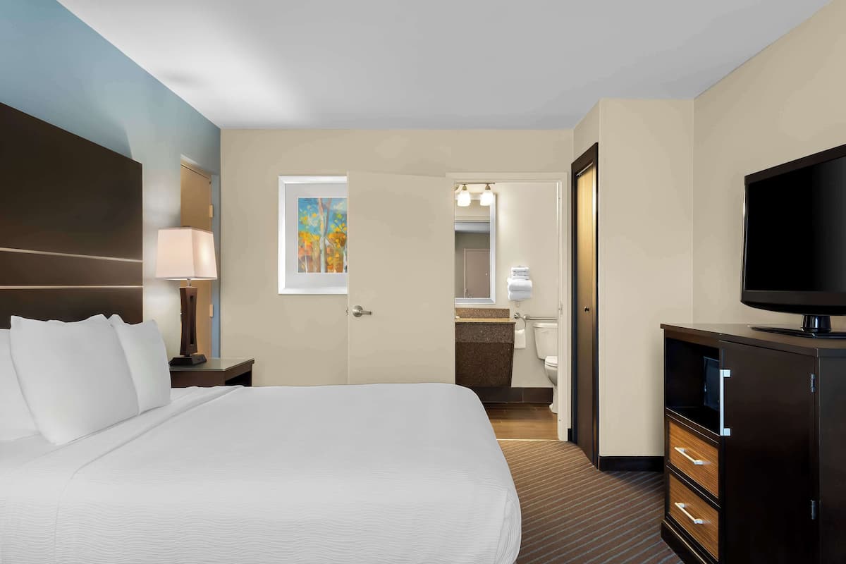 A hotel room with a large bed, a television, a desk with a lamp, and a bathroom visible through an open door.