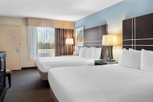A hotel room with two beds, a desk, a lamp, and a window with curtains.