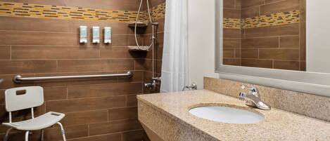 Une salle de bain équipée d’une douche, d’un lavabo, d’un miroir et d’un siège accessible aux personnes en fauteuil roulant.