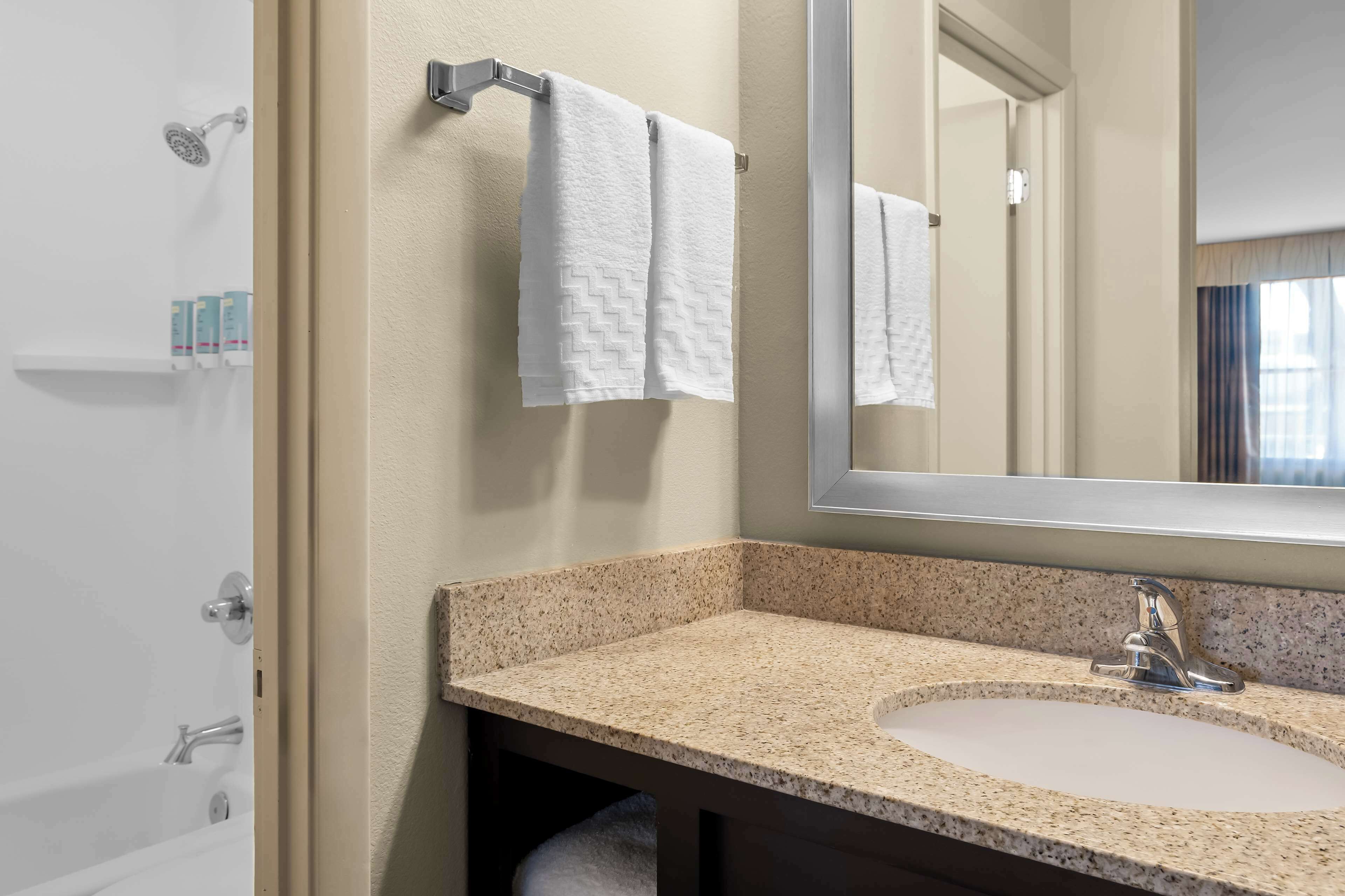 A bathroom with a granite countertop sink, a large mirror, and two white towels hanging on a towel rack.