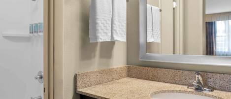 A bathroom with a granite countertop sink, a large mirror, and two white towels hanging on a towel rack.