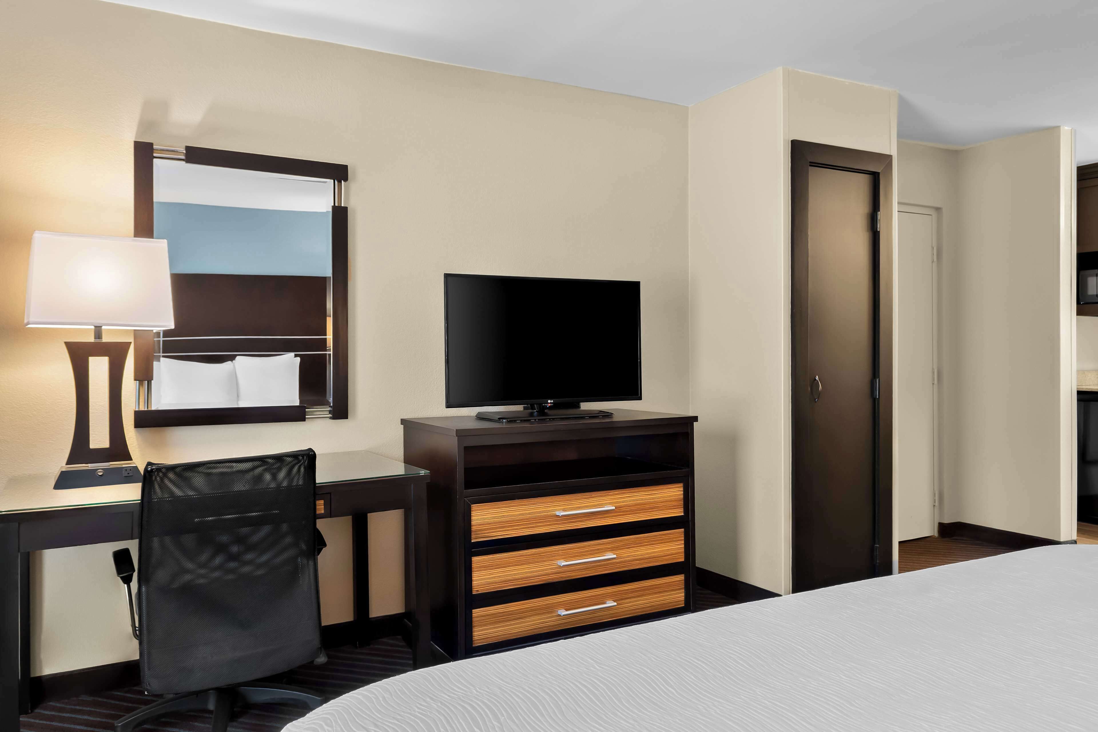 Habitación de hotel con cama, escritorio con lámpara, televisión, silla y armario.
