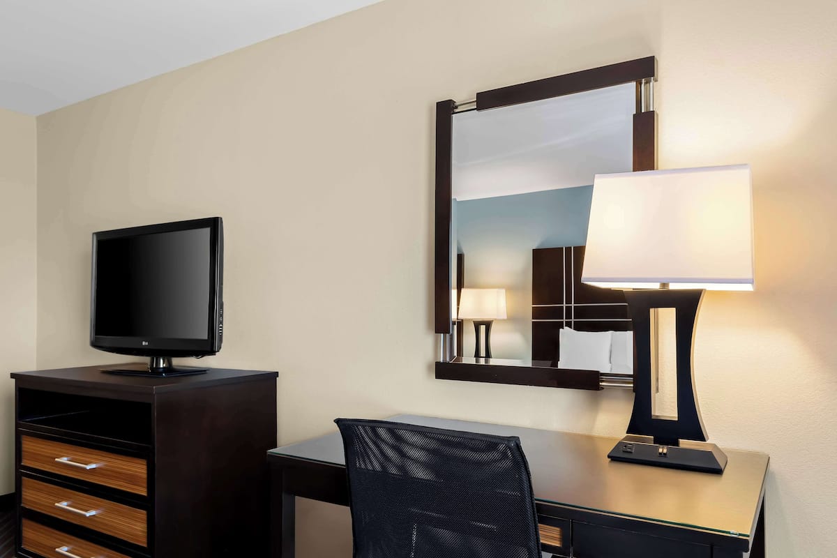 A hotel room with a desk, a television, a mirror, and a lamp.