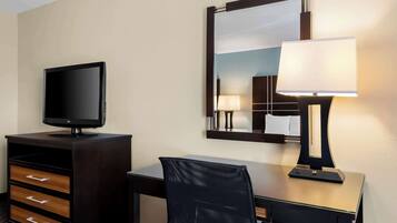 A hotel room with a desk, a television, a mirror, and a lamp.