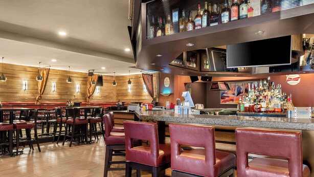 Zona de bar con diversas opciones de asientos, un televisor y una variedad de botellas en las estanterías.
