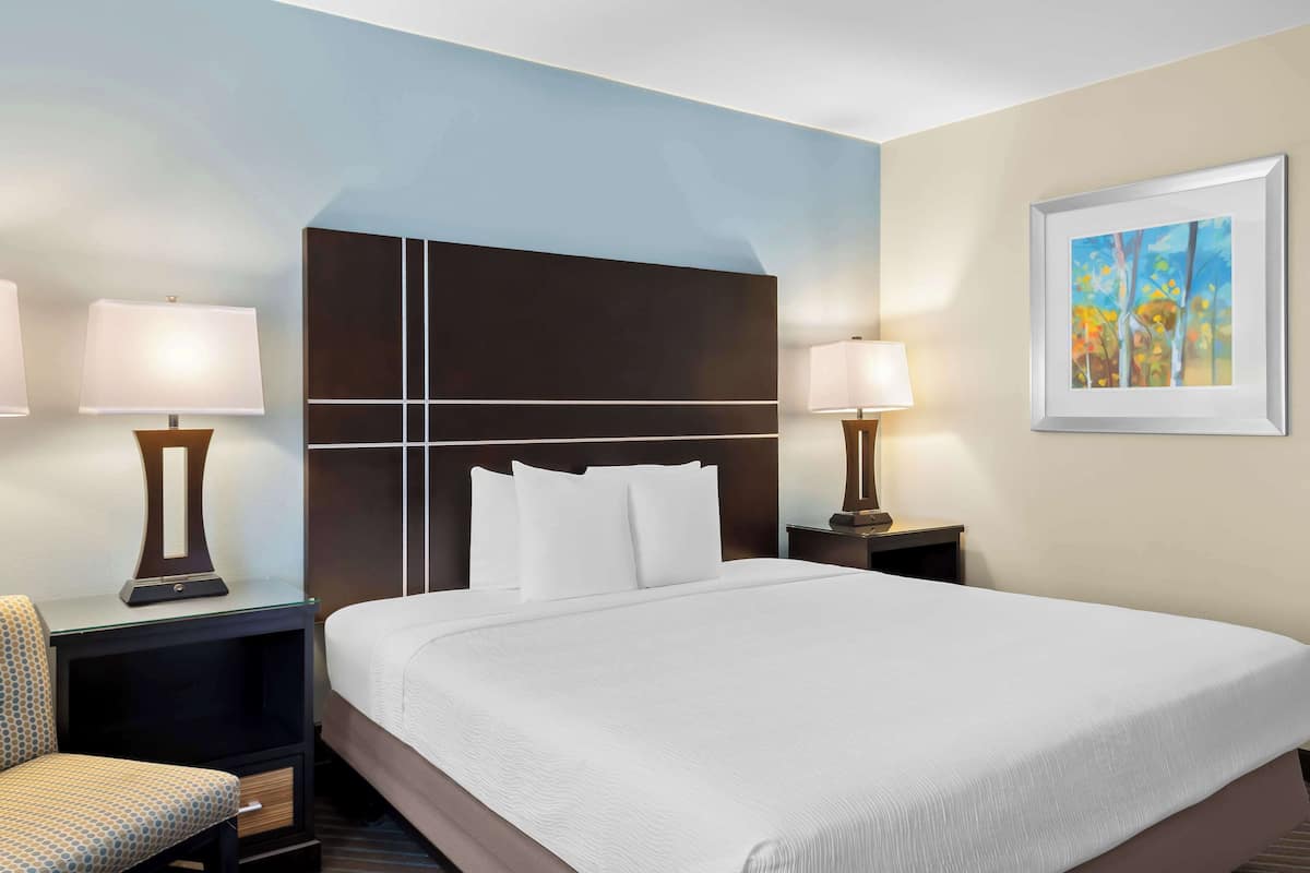 A hotel room with a large bed, two bedside tables with lamps, a chair, and a framed painting on the wall.
